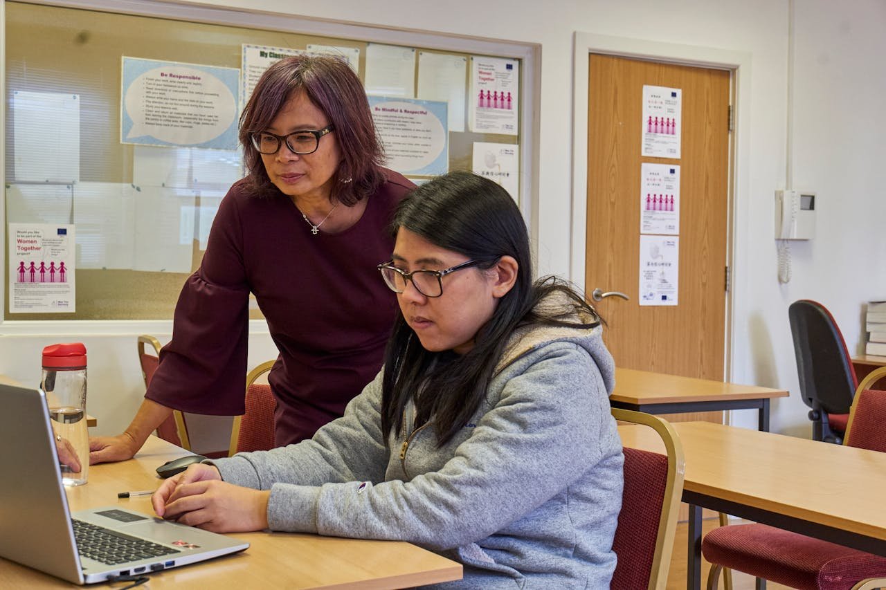 Two women collaborate and work together using a laptop in an office setting.
