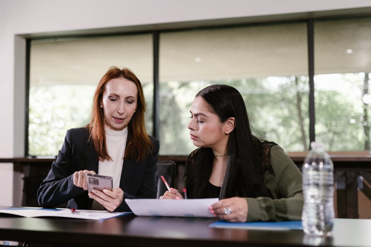 Two professional women collaborating with documents and smartphone in a meeting room.